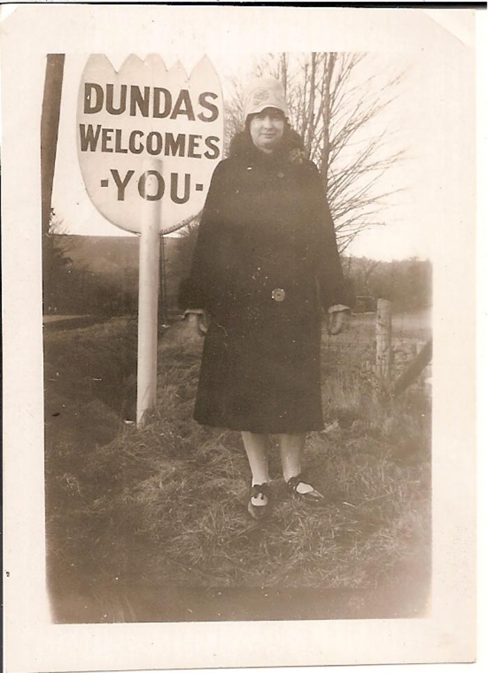 A woman stands next to a tulip-shaped sign that says "Dundas Welcomes You"